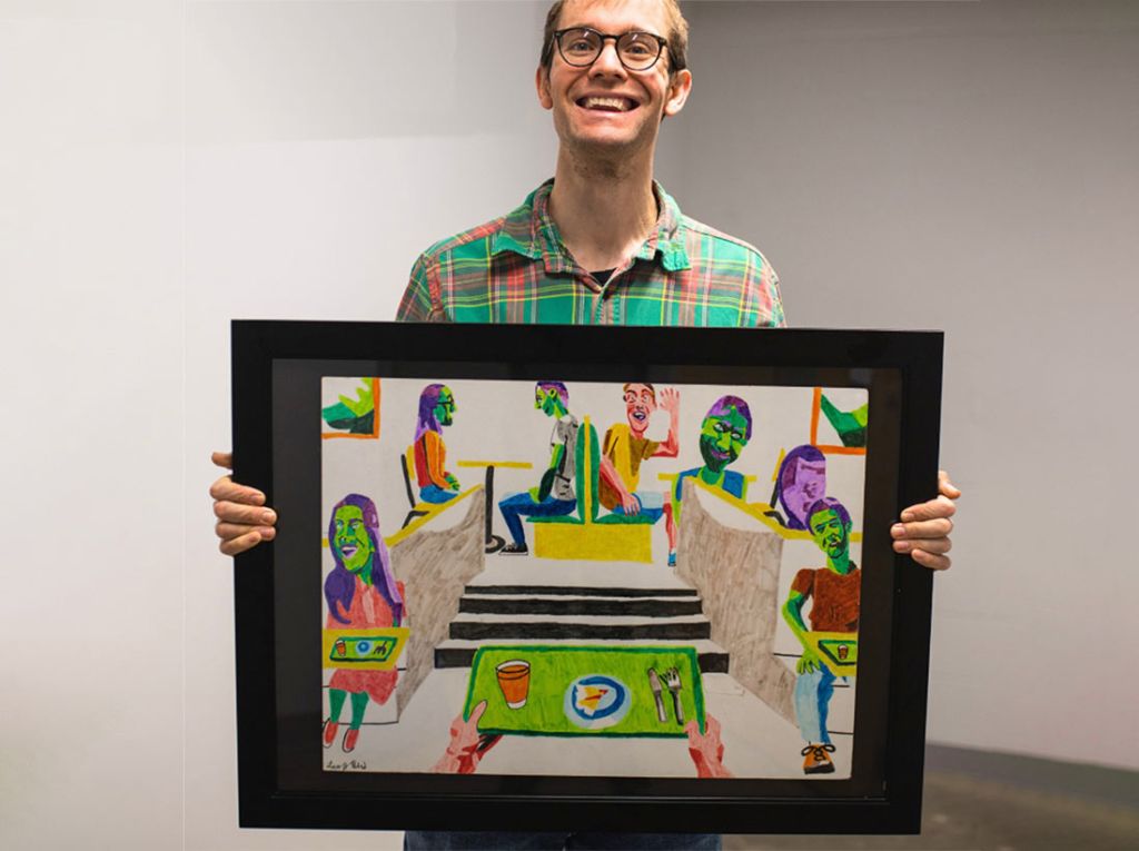 An artist holding his work (a drawing of colorful people at a cafeteria) and smiling